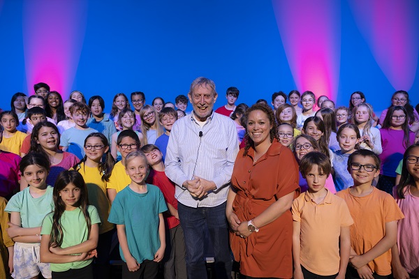 Pupils in colourful clothing surround Michael Rosen on stage